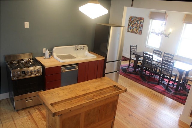 kitchen featuring appliances with stainless steel finishes, light hardwood / wood-style floors, an inviting chandelier, and sink