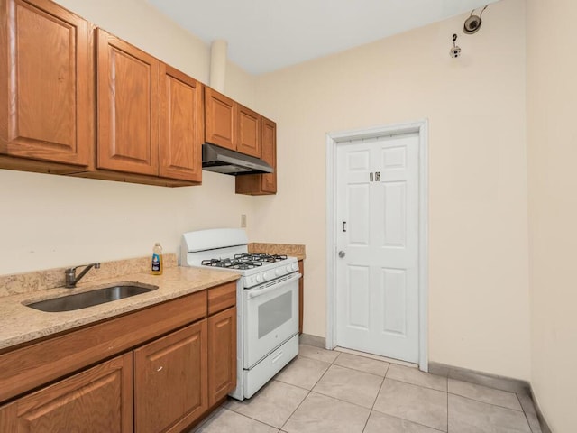 kitchen featuring light tile patterned flooring, light stone counters, white range with gas stovetop, and sink