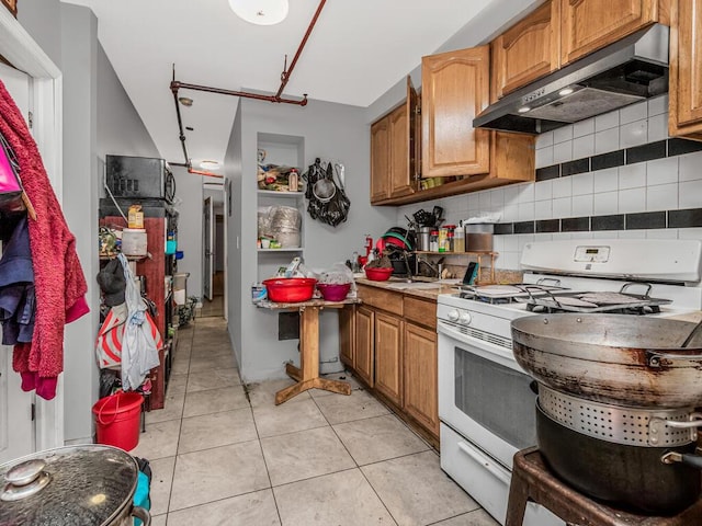 kitchen featuring decorative backsplash, white range with gas cooktop, sink, exhaust hood, and light tile patterned floors