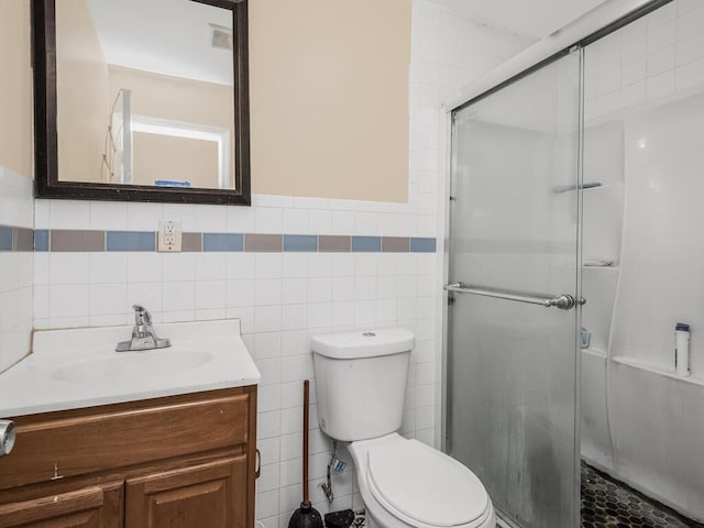 bathroom featuring vanity, toilet, tile walls, and a shower with shower door