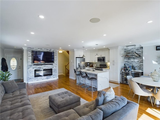 living room with light wood-type flooring, a stone fireplace, ornamental molding, and sink