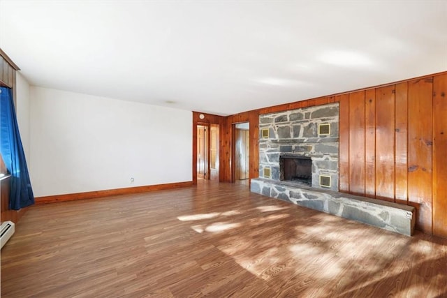 unfurnished living room featuring hardwood / wood-style floors, a stone fireplace, wooden walls, and a baseboard radiator