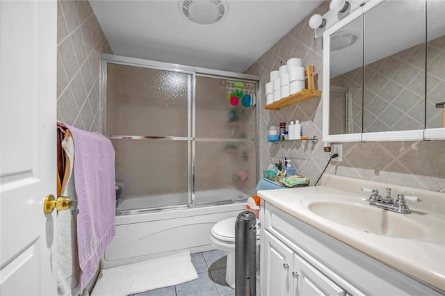 full bathroom with tile patterned floors, combined bath / shower with glass door, toilet, vanity, and tile walls