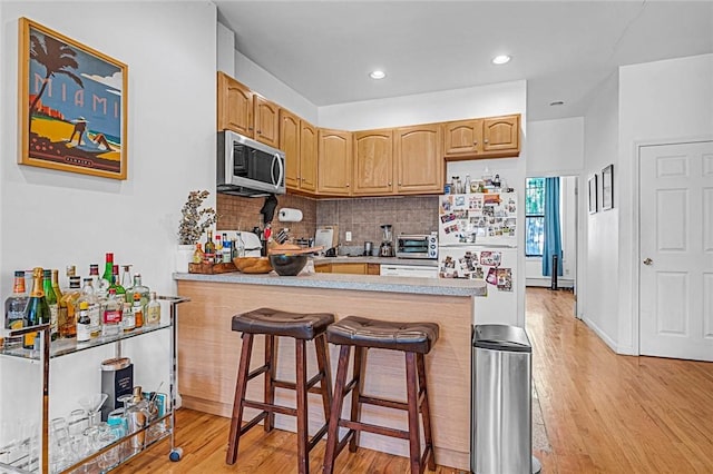 kitchen featuring white refrigerator, backsplash, kitchen peninsula, a kitchen bar, and light wood-type flooring