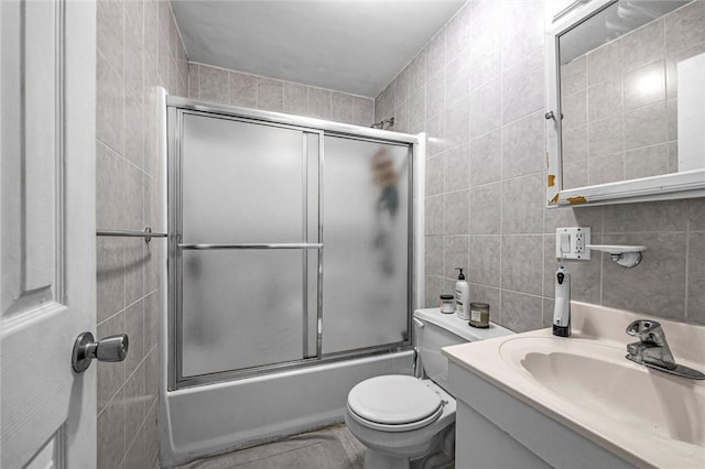 full bathroom with vanity, toilet, combined bath / shower with glass door, and tile walls