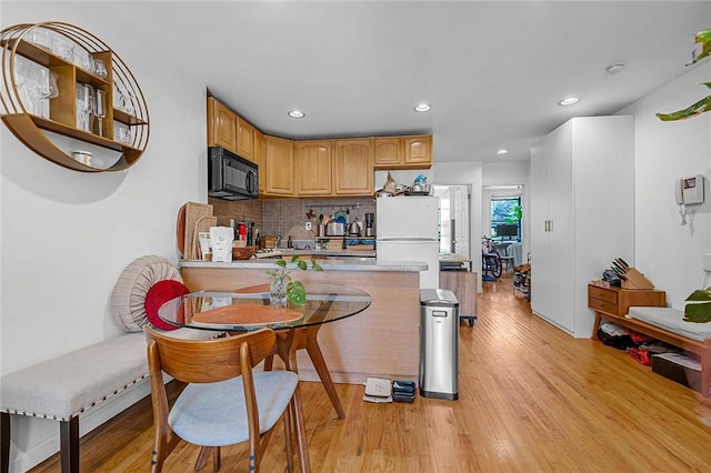 kitchen with white fridge, light hardwood / wood-style floors, kitchen peninsula, and backsplash