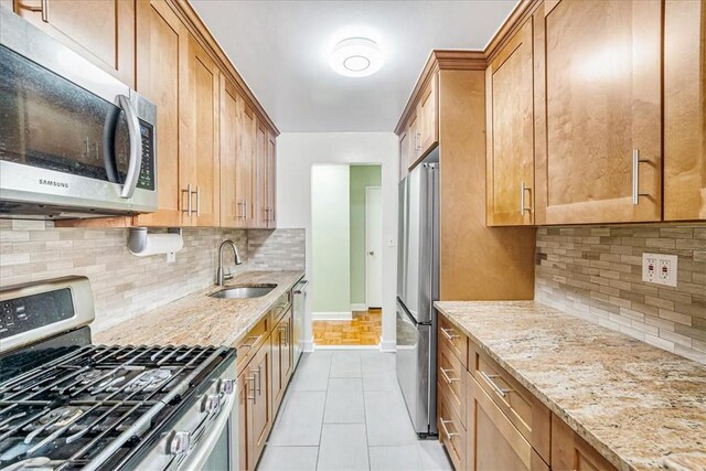 kitchen featuring appliances with stainless steel finishes, tasteful backsplash, light stone counters, sink, and light tile patterned floors