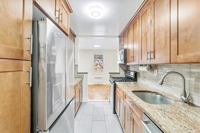 kitchen featuring light stone counters, stainless steel appliances, sink, radiator heating unit, and light tile patterned flooring