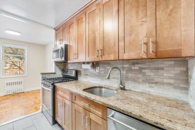 kitchen featuring light stone countertops, radiator heating unit, sink, stainless steel appliances, and decorative backsplash