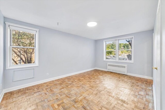 unfurnished room with plenty of natural light, radiator heating unit, and light parquet floors