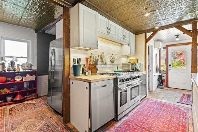 kitchen with a healthy amount of sunlight, white cabinetry, wooden counters, and stainless steel appliances