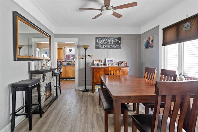 dining area featuring ceiling fan, a fireplace, and light wood-type flooring