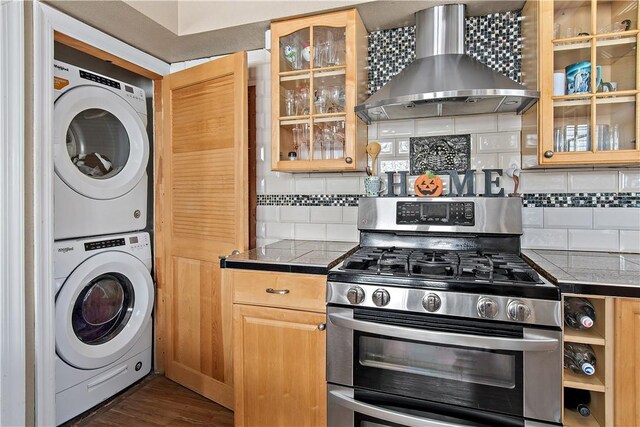 kitchen with stacked washer and clothes dryer, wall chimney range hood, decorative backsplash, dark hardwood / wood-style floors, and gas stove