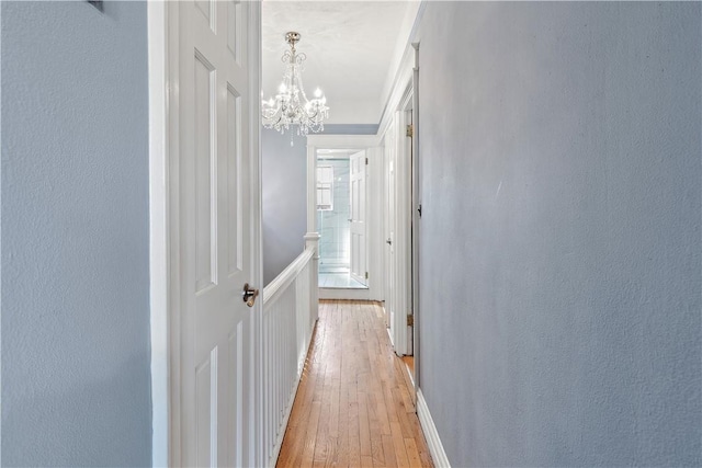 corridor with light hardwood / wood-style flooring and an inviting chandelier