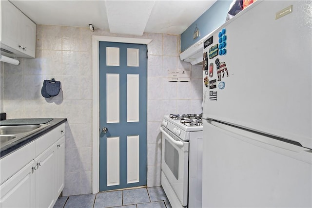 kitchen featuring white appliances, sink, light tile patterned floors, tile walls, and white cabinetry