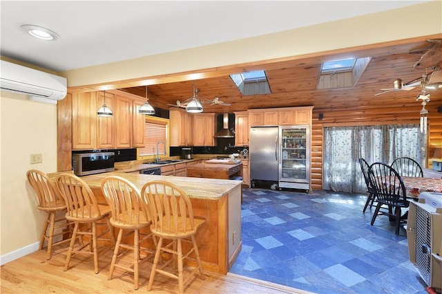 kitchen with a breakfast bar, a skylight, wall chimney exhaust hood, appliances with stainless steel finishes, and kitchen peninsula