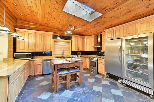 kitchen with appliances with stainless steel finishes, a skylight, light stone counters, wall chimney exhaust hood, and hanging light fixtures