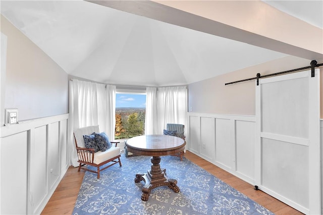 sitting room with a barn door, light hardwood / wood-style floors, and lofted ceiling