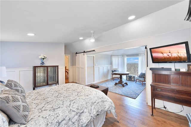 bedroom featuring a barn door, ceiling fan, lofted ceiling, and hardwood / wood-style flooring