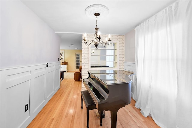 misc room featuring an inviting chandelier, light hardwood / wood-style flooring, and brick wall