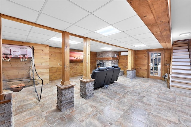 basement with a wall mounted AC, a drop ceiling, and wood walls