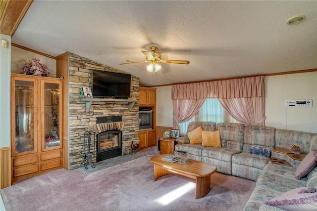 carpeted living room with a textured ceiling, vaulted ceiling, ceiling fan, crown molding, and a stone fireplace