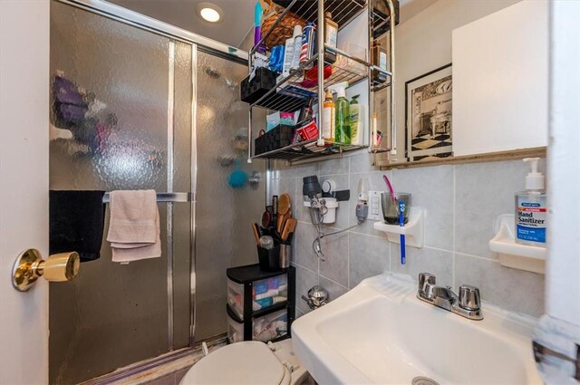 bathroom featuring tasteful backsplash, toilet, a shower with shower door, and sink