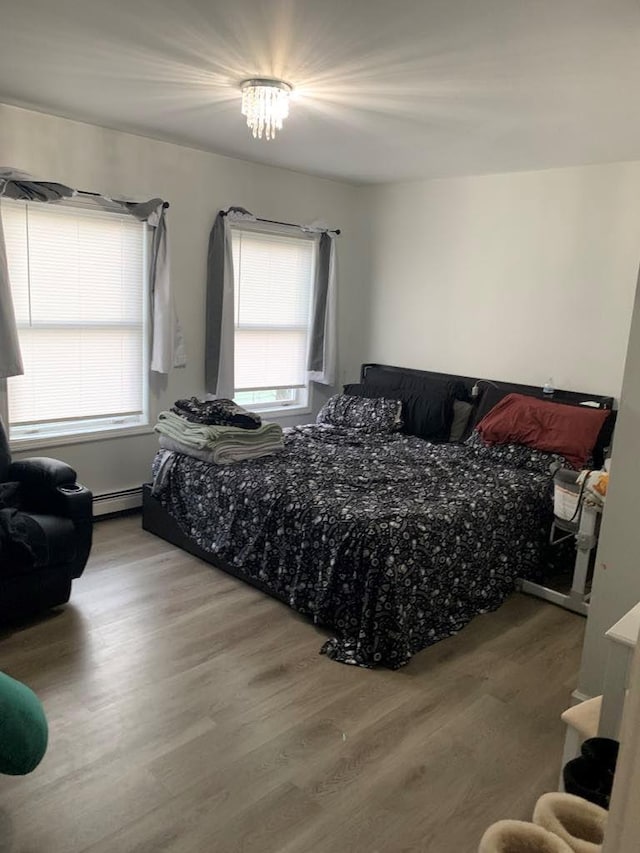 bedroom featuring wood-type flooring, a baseboard radiator, and an inviting chandelier