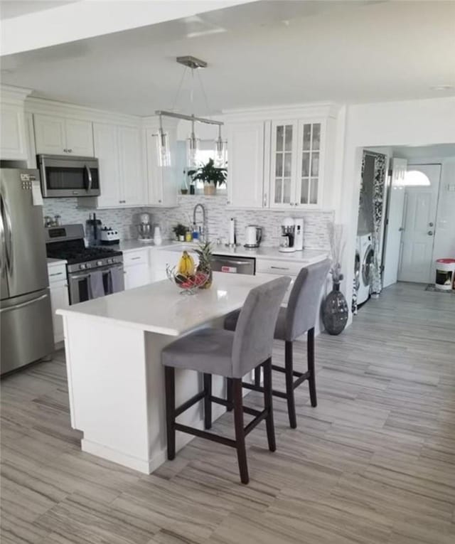 kitchen featuring washer and dryer, hanging light fixtures, white cabinets, and stainless steel appliances