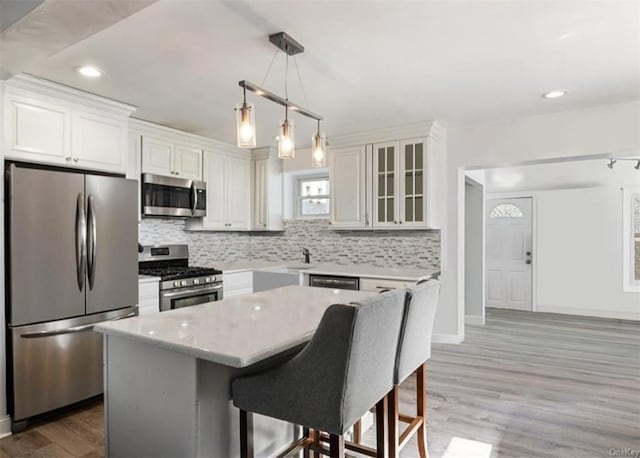 kitchen featuring stainless steel appliances, a kitchen island, hardwood / wood-style floors, decorative light fixtures, and white cabinets