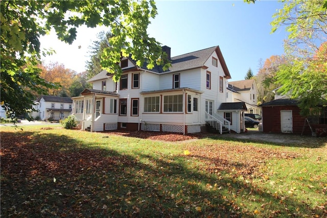 rear view of house featuring a lawn, a sunroom, and a storage unit