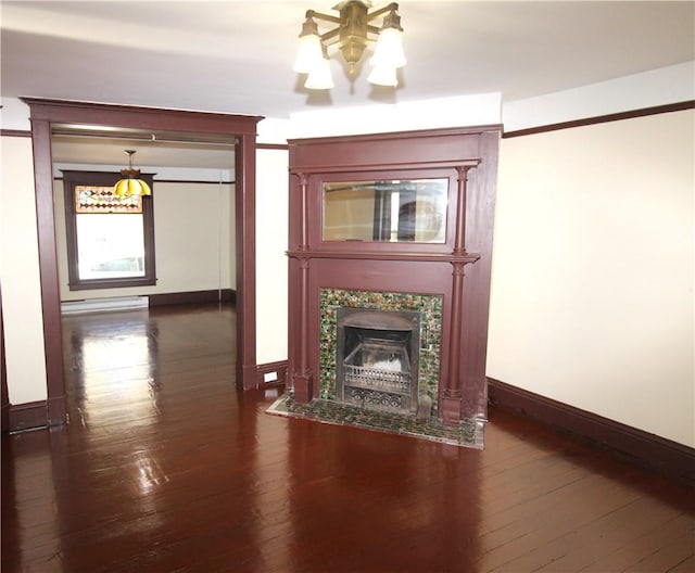 unfurnished living room featuring a fireplace, dark wood-type flooring, a chandelier, and a baseboard heating unit