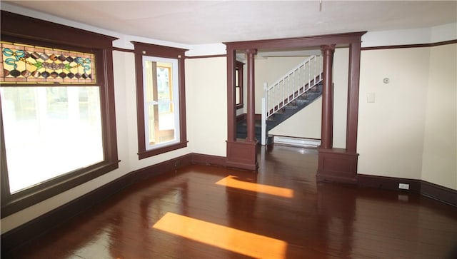 unfurnished room featuring ornate columns, dark hardwood / wood-style flooring, and a baseboard heating unit