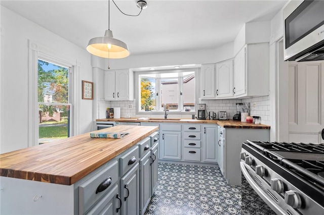 kitchen with hanging light fixtures, plenty of natural light, wooden counters, and appliances with stainless steel finishes