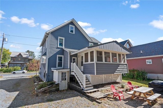 rear view of property featuring an outdoor fire pit and a sunroom