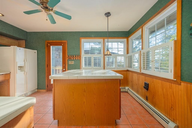 kitchen featuring tile countertops, white refrigerator with ice dispenser, baseboard heating, decorative light fixtures, and a kitchen island