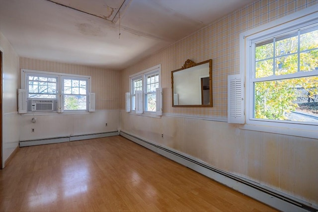 empty room with hardwood / wood-style floors, a wealth of natural light, and a baseboard heating unit