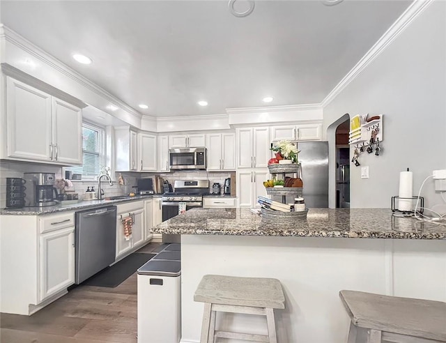 kitchen with sink, stainless steel appliances, dark stone counters, a breakfast bar, and white cabinets