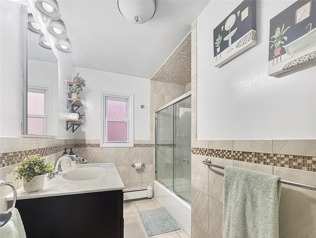 bathroom with tile patterned flooring, enclosed tub / shower combo, a baseboard heating unit, vanity, and tile walls