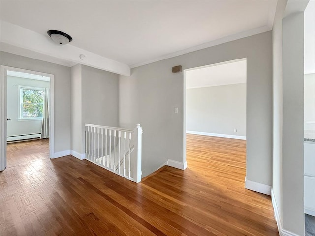 spare room featuring wood-type flooring, crown molding, and baseboard heating