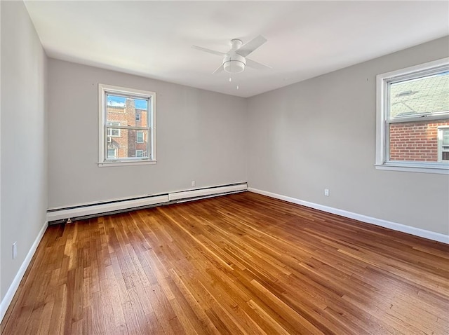 empty room featuring ceiling fan, wood-type flooring, baseboard heating, and a wealth of natural light