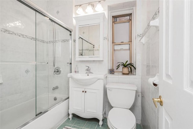 full bathroom with vanity, combined bath / shower with glass door, tile patterned flooring, toilet, and tile walls