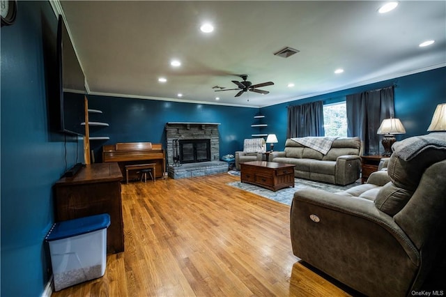 living room with ceiling fan, a stone fireplace, wood-type flooring, and ornamental molding