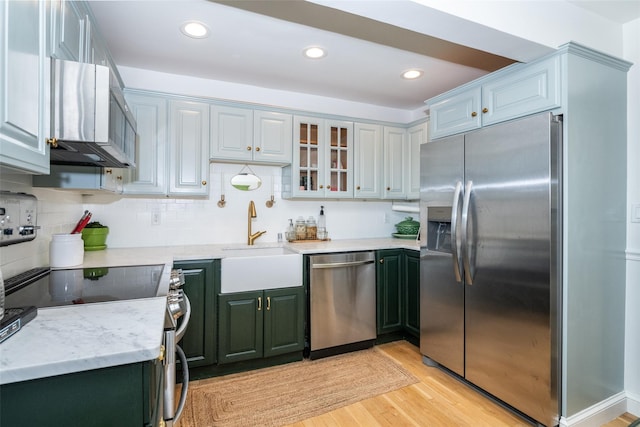 kitchen featuring appliances with stainless steel finishes, tasteful backsplash, light stone counters, sink, and light hardwood / wood-style flooring