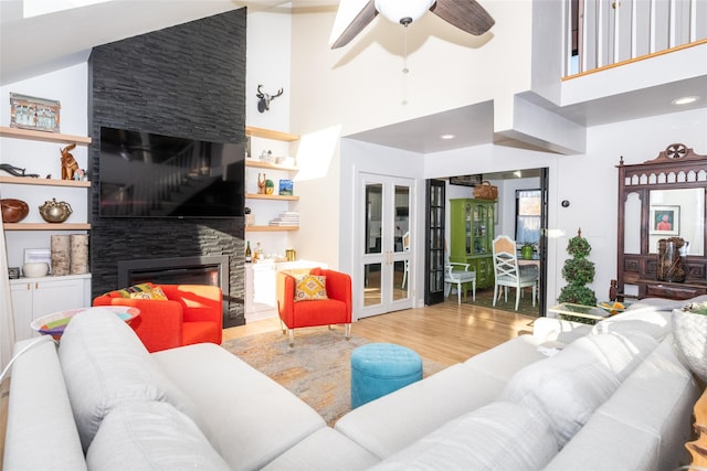 living room featuring ceiling fan, french doors, light hardwood / wood-style flooring, high vaulted ceiling, and a fireplace