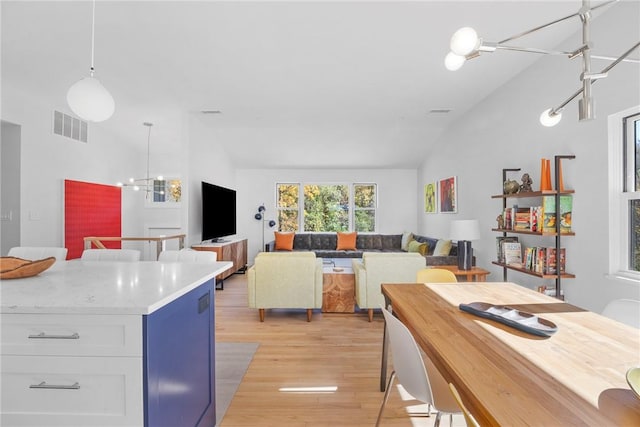 kitchen featuring white cabinetry, pendant lighting, a chandelier, lofted ceiling, and light hardwood / wood-style floors