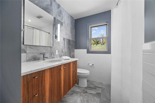 bathroom with a shower with curtain, vanity, toilet, and tile walls