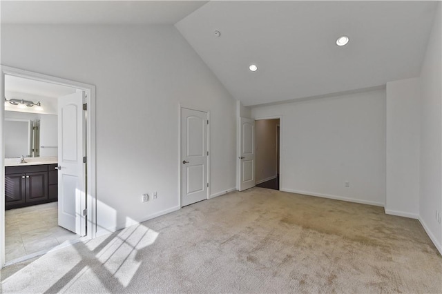 unfurnished bedroom with ensuite bathroom, sink, high vaulted ceiling, and light colored carpet