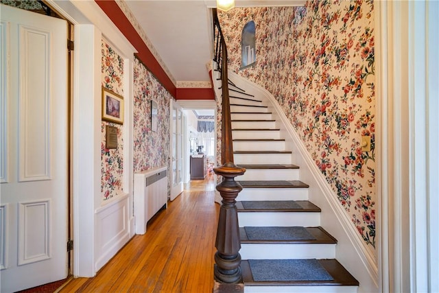 stairs featuring wood-type flooring, radiator heating unit, and ornamental molding