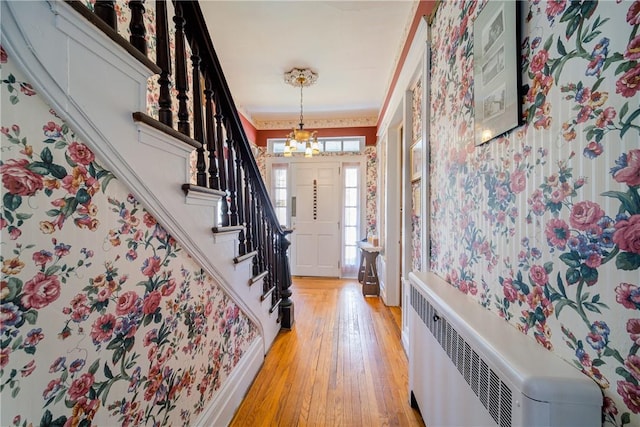 entrance foyer featuring crown molding, light hardwood / wood-style flooring, an inviting chandelier, and radiator heating unit